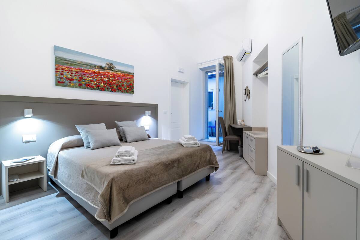 A modern hotel room with a large bed, bedside lamps, a desk, and a mirror.