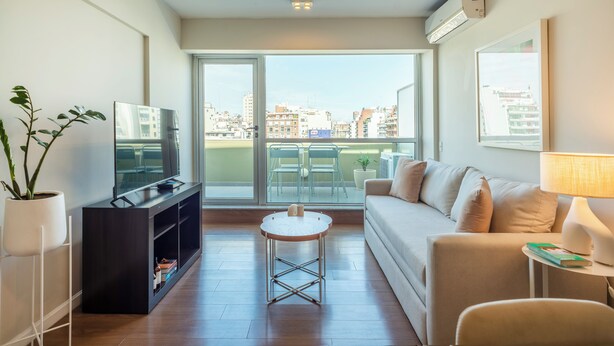 Una sala de estar moderna con un sofá, un televisor, una mesita redonda y una planta en maceta.
