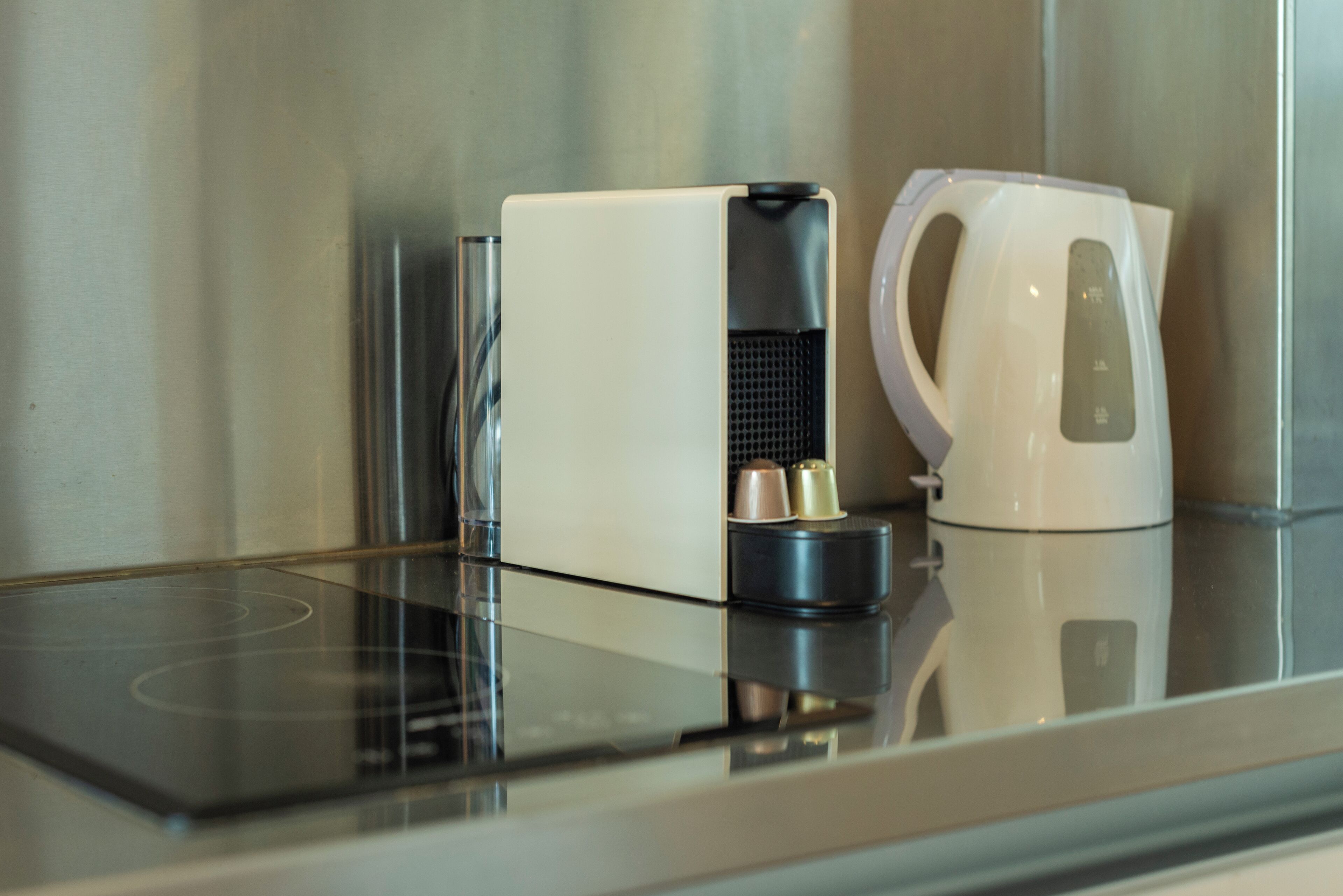 Una cocina moderna con cafetera integrada y hervidor sobre una encimera de cristal.