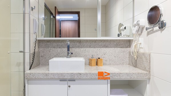 A bathroom with a white sink, granite countertop, and a mirror above the sink. There is a hairdryer and a phone on the wall. - Seu Refúgio à Beira-Mar TRP1608 (Recife)
