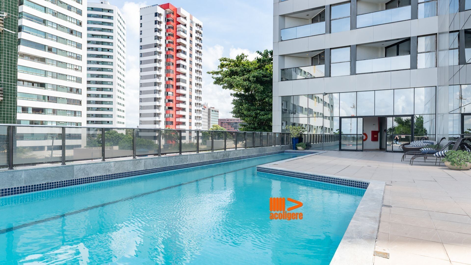 A swimming pool with a glass barrier, surrounded by modern buildings and outdoor seating.