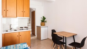 Une cuisine compacte avec des meubles en bois, un plan de travail blanc et un petit coin repas comprenant deux chaises et une table.