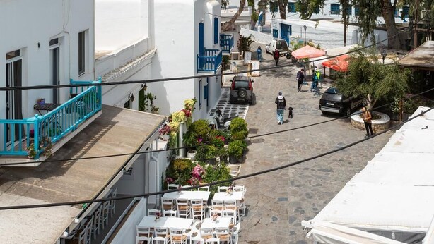 Une rue étroite bordée de bâtiments blancs, avec des terrasses et des arbres.