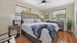 Un dormitorio con cama, mesitas de noche, ventilador de techo y ventana con persianas.