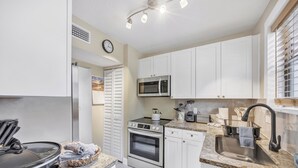 Una cocina moderna con armarios blancos, electrodomésticos de acero inoxidable, encimera de granito y ventana con persianas.