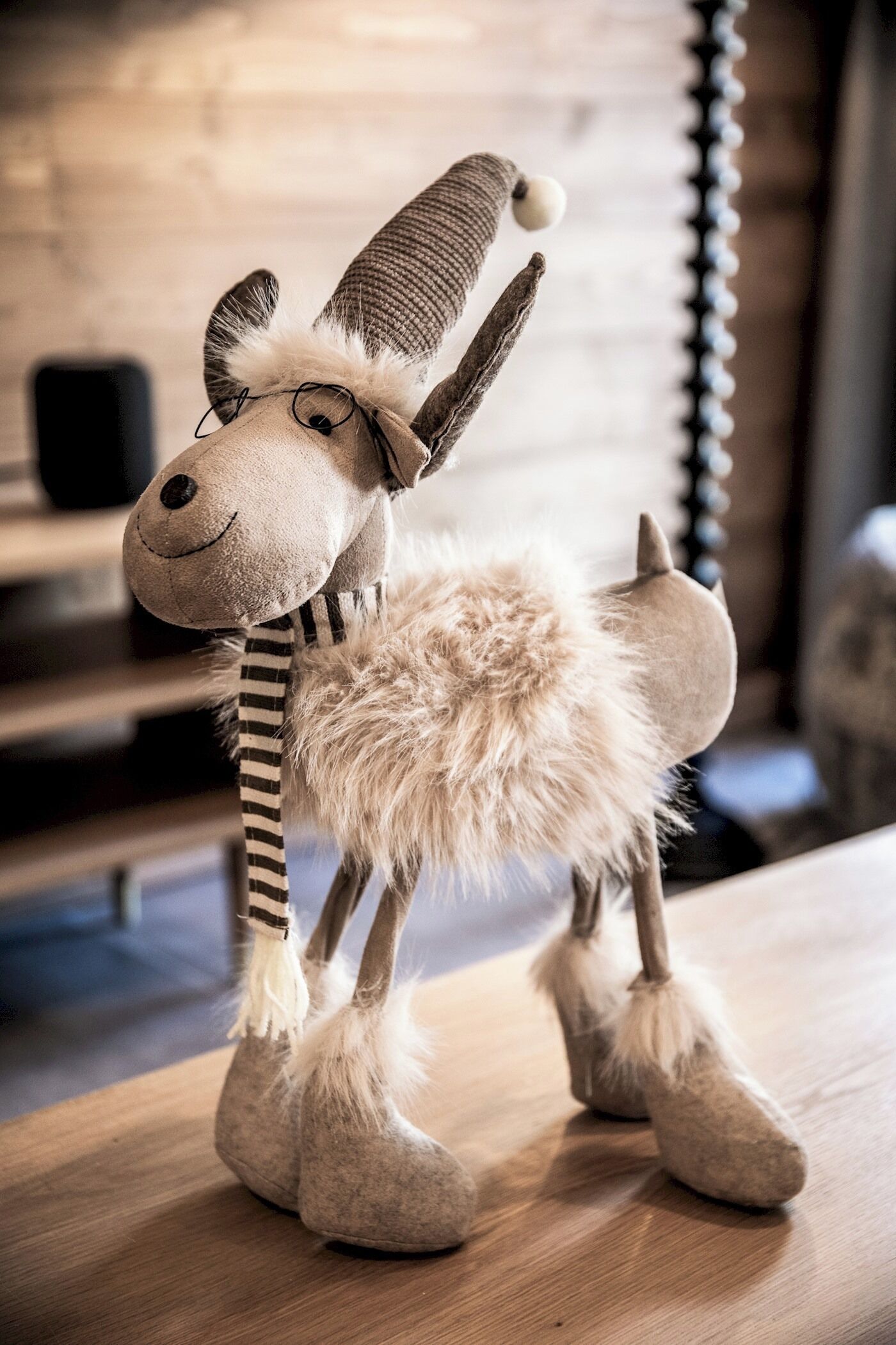 Een zacht knuffeldiertje met een gestreepte sjaal en pluizige pootjes, staand op een houten ondergrond.