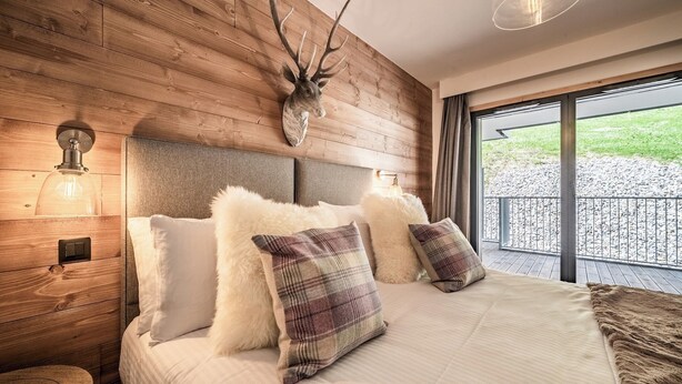 A bedroom with a wooden headboard, plush pillows, and a large window with a view of a gravel path.