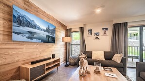 A modern living room with a large TV, wooden paneling, a sofa, a coffee table, and a view of a balcony.