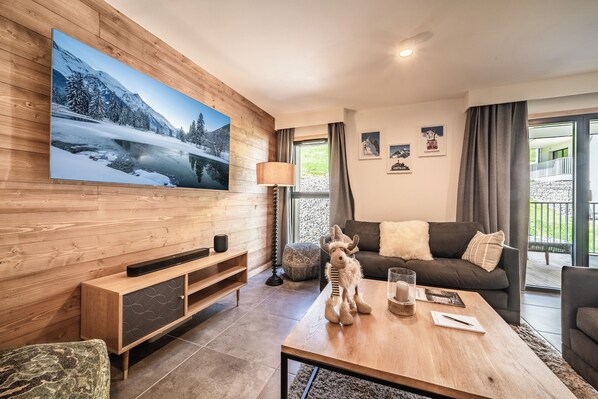 A modern living room with a large TV, wooden paneling, a sofa, a coffee table, and a view of a balcony.