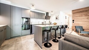 A modern kitchen with grey cabinets, a central island with bar stools, and a wooden accent wall.