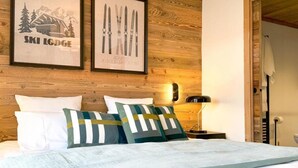 Une chambre à coucher avec une tête de lit en bois, un lit recouvert d’une literie blanche et agrémenté d’oreillers à rayures, un tableau encadré représentant des skis et une lampe fixée au mur.