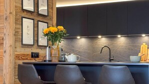 Une cuisine moderne avec un mur d’accent en bois, des armoires noires et un coin bar équipé de trois chaises noires.