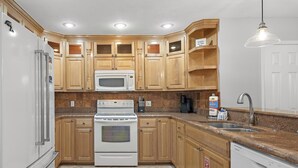 A kitchen with wooden cabinets, a white refrigerator, a microwave, an oven, a dishwasher, and a sink.