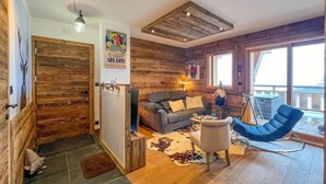 A cozy cabin interior with a wooden door, a sofa, a rocking chair, and a large window.