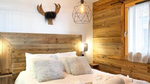 A wooden-paneled bedroom with a large bed, two bedside tables, a wall-mounted deer head, and a geometric pendant light.
