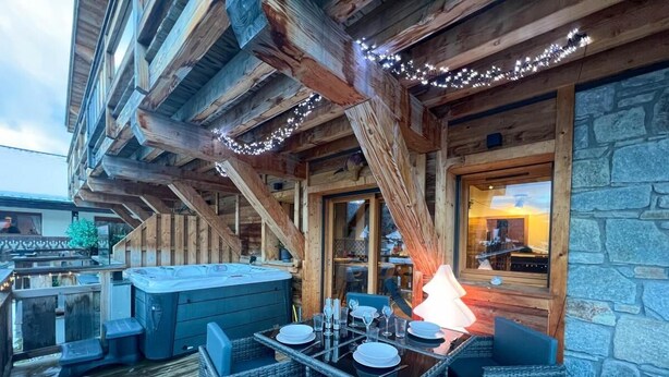 An outdoor patio with a table set for dining, a hot tub, and wicker furniture.