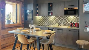 A modern kitchen with a dining area, featuring a wooden ceiling, grey cabinets, and a patterned backsplash.