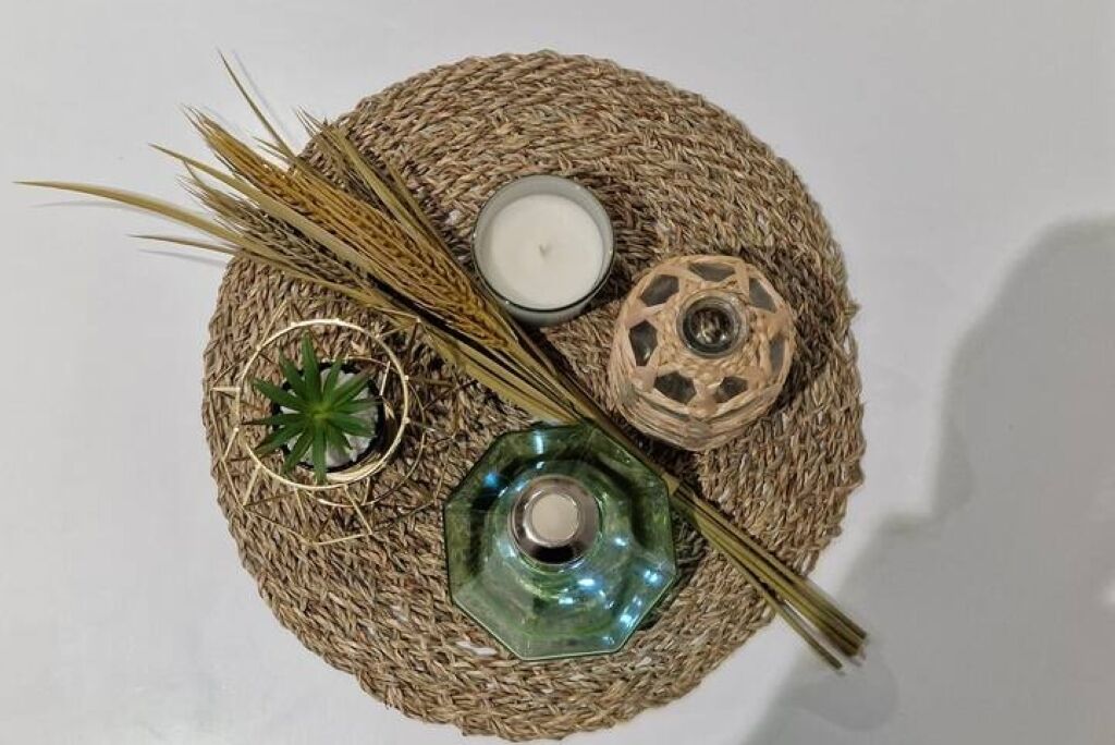 A round woven mat with a candle, a glass container, and dried grass.
