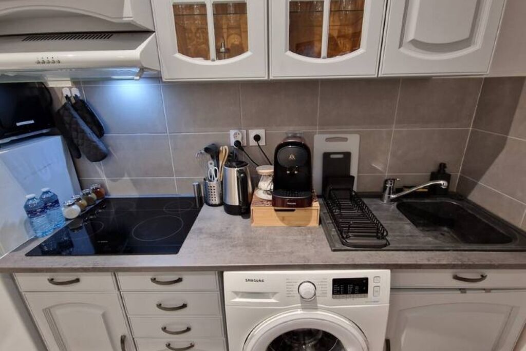 Uma cozinha compacta com máquina de lavar e secar integradas, fogão, cafeteira e pia.