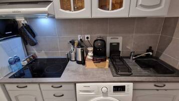 Uma cozinha compacta com máquina de lavar e secar integradas, fogão, cafeteira e pia.