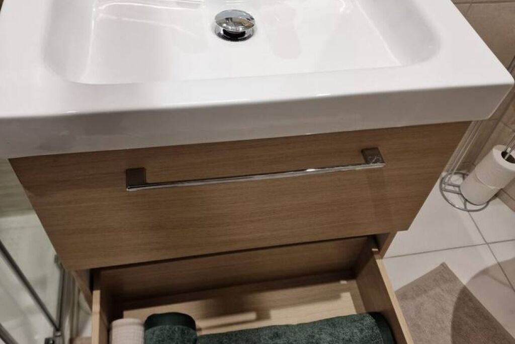 A bathroom with a white sink, a wooden drawer below, and a toilet paper holder to the right.