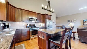 A modern kitchen with wooden cabinets, stainless steel appliances, a granite countertop, and a dining area with leather chairs. - Modern Mountain Retreat/Incredible Mountain Views/Stylish Kitchen/Spotless (Estes Park)