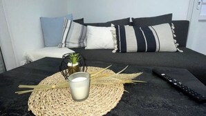 A neatly arranged bed with a black headboard, a bedside table with a candle and a small plant, and a remote control on the bed.