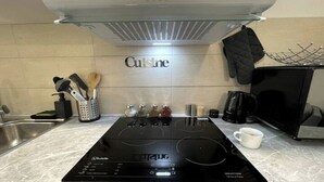 A kitchen with a black induction cooktop, a stainless steel range hood, and a backsplash with the word "Cuisine".