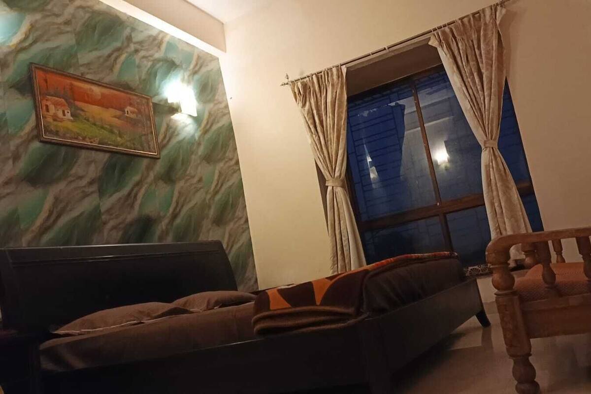 Una sala de estar con un sofá, una silla de madera, un televisor y una ventana con cortinas.