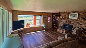 A spacious living room with a large window, a fireplace, and a television. - Pinedale's Mountain Vista (Pinedale)