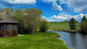 A wooden gazebo with a sloped roof and open sides, surrounded by lush green grass and trees. - Pinedale's Mountain Vista (Pinedale)