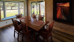 A dining room with a wooden table and chairs, large windows, and a framed picture on the wall. - Pinedale's Mountain Vista (Pinedale)