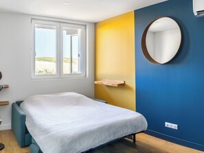 A bedroom with a bed, a window, a mirror, and a wall with a shelf.