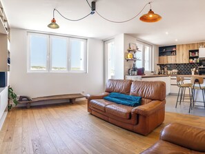 A spacious living room with a leather sofa, wooden flooring, and large windows.
