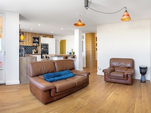 A modern living room with a brown leather sofa, a brown leather armchair, and a blue throw blanket.