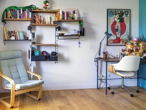 A room with a desk, chair, bookshelf, and a wall-mounted shelf.
