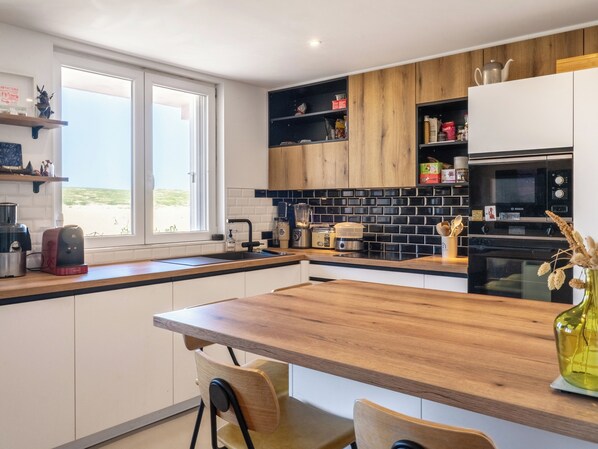 A modern kitchen with a wooden countertop, built-in appliances, and a view through the window.
