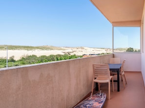 A balcony with a table and chairs, overlooking a beach and dunes.