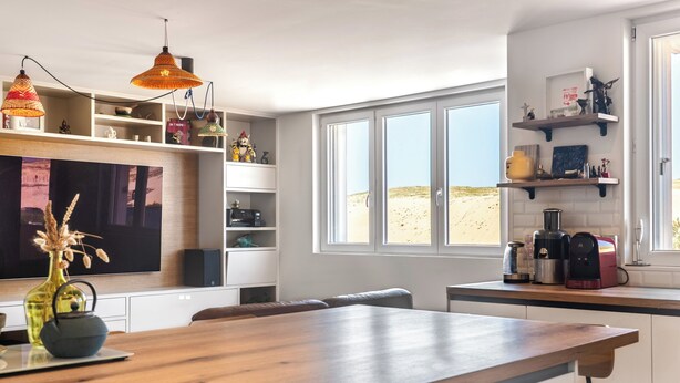 A modern kitchen with a wooden island, white cabinetry, and a large window with a view of the desert. - Hossegor Les Semis in front of the Gravière dune (Soorts-Hossegor)
