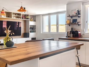 A modern kitchen with a wooden island, white cabinetry, and a large window with a view of the desert.