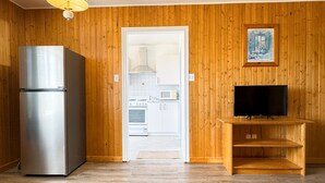 Una habitación con paneles de madera, un refrigerador de acero inoxidable, un microondas, un horno y un televisor sobre un soporte de madera.