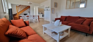 Un salon avec un canapé, une table basse et un téléviseur. Un escalier mène à une cuisine.