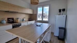A modern kitchen with wooden cabinets, a central island, a built-in oven, and a large window providing natural light. - Pretty and bright renovated house in the center of Trégunc with enclosed garden (Trégunc)