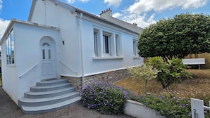 A white two-story house with a front entrance, a set of stairs, and a garden with purple flowers. - Pretty and bright renovated house in the center of Trégunc with enclosed garden (Trégunc)