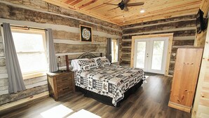 A log cabin bedroom with a bed, wooden dresser, and a ceiling fan.