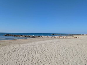 Ein sandiger Strand mit einem steinernen Wellenbrecher und ruhiger See.