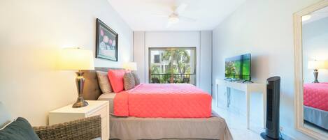 A bedroom with a bed, bedside table, lamp, TV, and a large window.