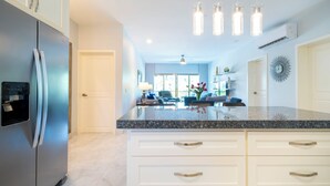 A modern kitchen with a stainless steel refrigerator, white cabinetry, granite countertops, and pendant lighting. - Luxury 2BR Condo with Pool - Paseo del Sol Playacar (Playa del Carmen)