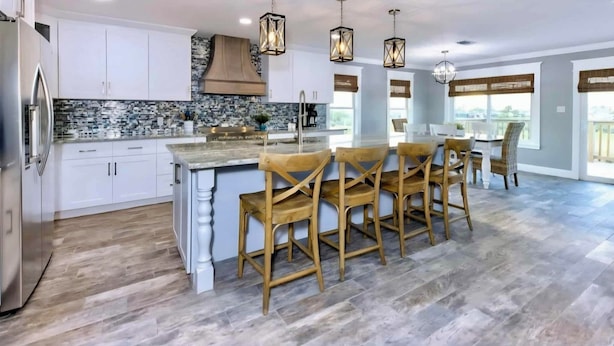 Una cocina moderna con armarios blancos, una isla central y sillas de madera.