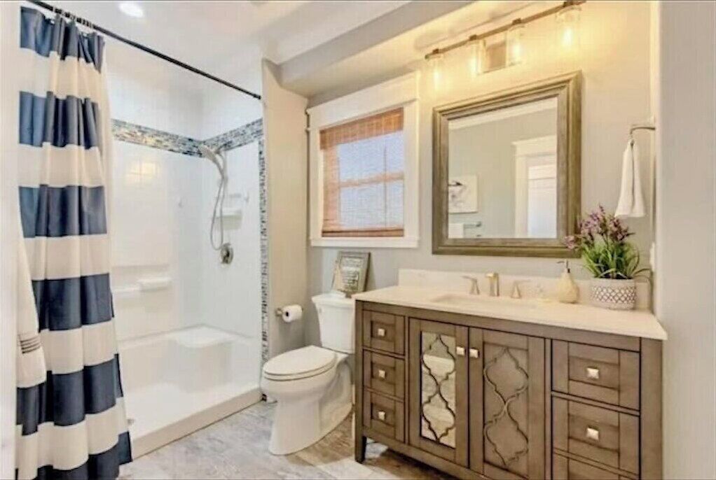 A bathroom with a glass shower enclosure, a toilet, a vanity with a mirror, and a window.